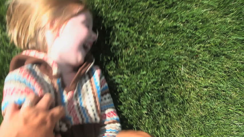 Point-of-view shot of a father tickling his daughter on the grass. Includes audio 