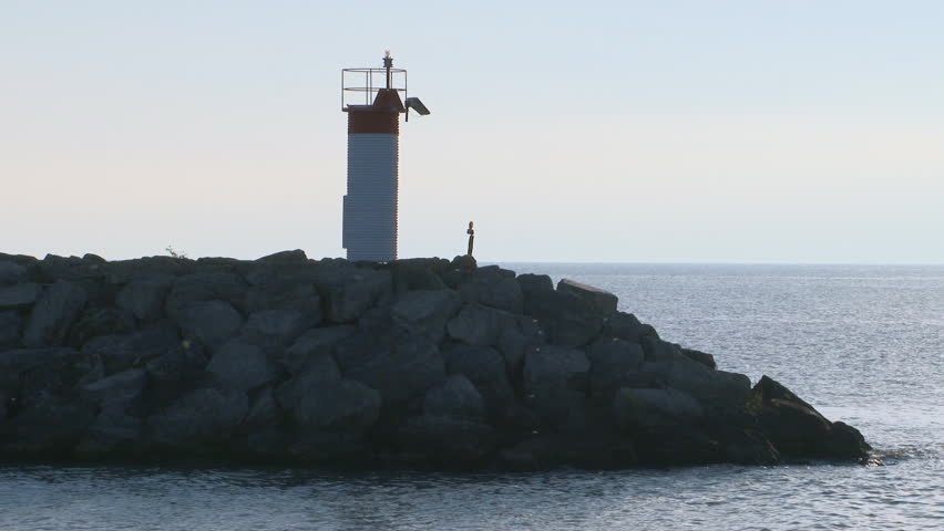 Backlit harbor break wall beacon at sunrise