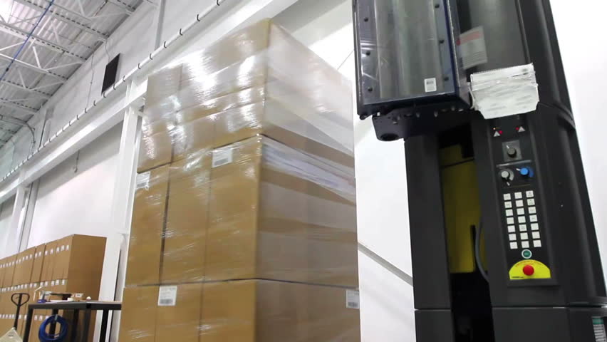 A shrink wrap machine covers a large stack of boxes 