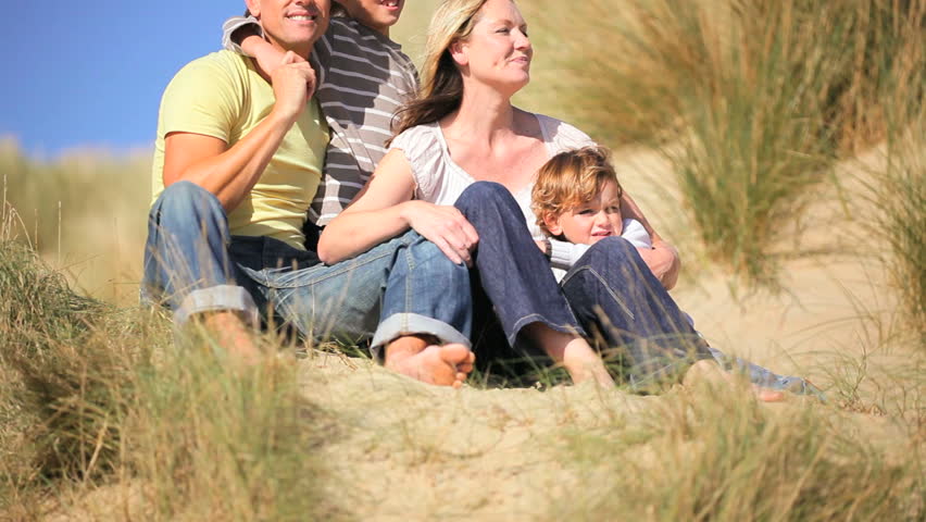 Attractive young caucasian family enjoying time together & the children having fun playing in sand dunes