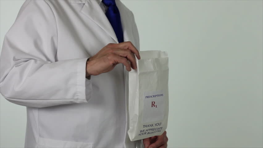 A pharmacist drops two bottles of prescription drugs into a paper bag and offers it to the camera