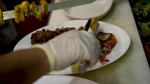 Chef slides chicken kabob off of a skewer onto a plate with beef kabob and rice with saffron.