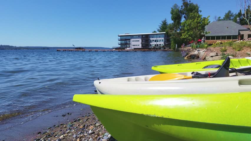 Three kayaks in closeup laying by the seashore during summer, people sunbathing in background