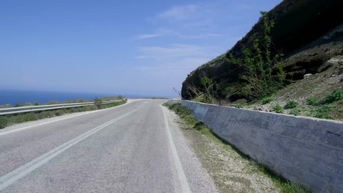 Pov shot of car driving on country road over a mountain with ocean and sea down in background