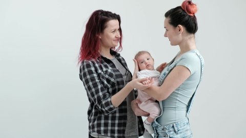 480px x 270px - Two young women with dyed red hair and in casual clothes with a baby on a  white background. same-sex marriage and adoption, homosexual lesbian couple.