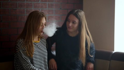 Nudist Smoking Outdoors - Teenage girls smoking an electronic cigarette in vape bar. bad habit that  is harmful to health. young pretty white caucasian teens vaping indoors.