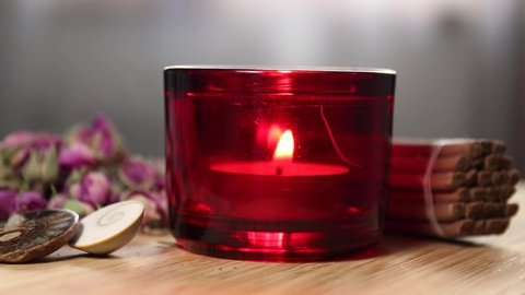 Tea Light Candle In A Red Glass With Dried Roses Stones And Incence Sticks Around On A Wood Desk