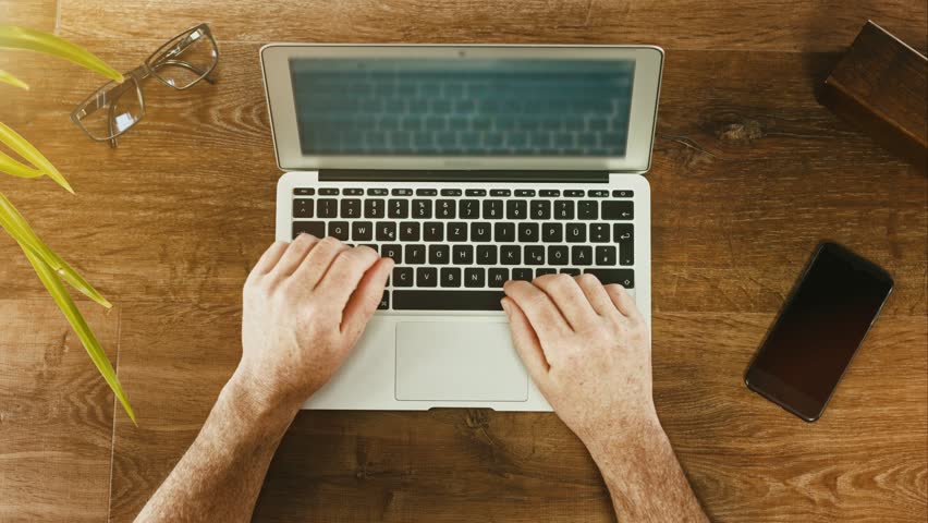 Desk Top View businessman typing on his laptop on a wooden desk table. top view Desk Top View businessman typing on his laptop on a wooden desk table. top view