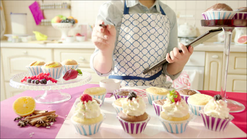 Woman Decorating Cupcakes woman decorating cup-cakes with sprinkling and berries / shot of Woman Decorating Cupcakes woman decorating cup-cakes with sprinkling and berries / shot of