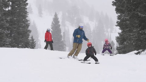 Parents and their children ski to camera together on snowy winter day at Alta Ski Area, Utah.