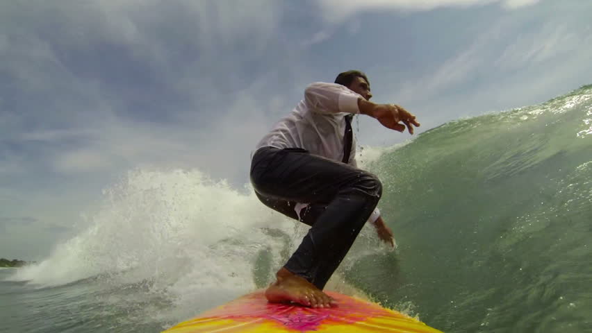 Cheerful businessman on surf board rides a tropical ocean wave