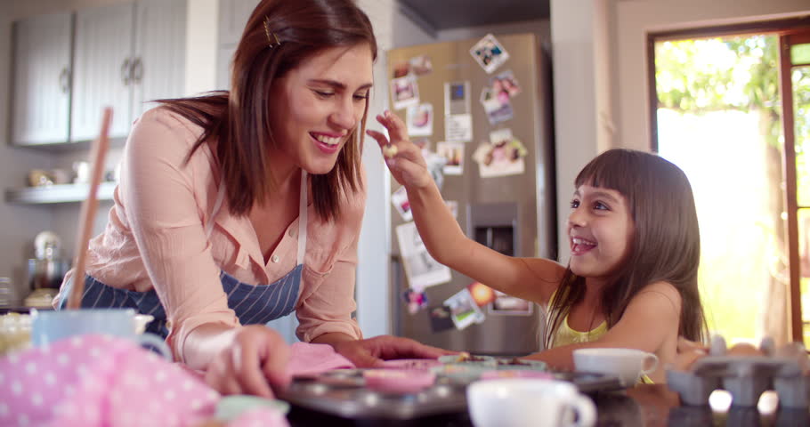 Laughing mom and daughter having fun together with the cupcake dough they are making in the kitchen while baking in Slow Motion